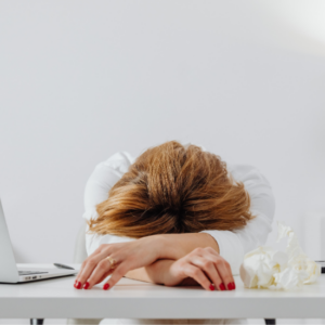 Donna seduta alla scrivania con la testa appoggiata sulle braccia, visibilmente stanca, accanto a un laptop e fazzoletti.